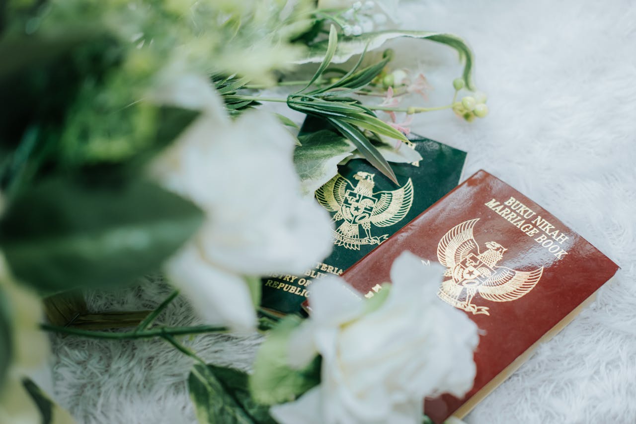 contact-img Close-up of Indonesian marriage books surrounded by a floral arrangement on a soft surface.