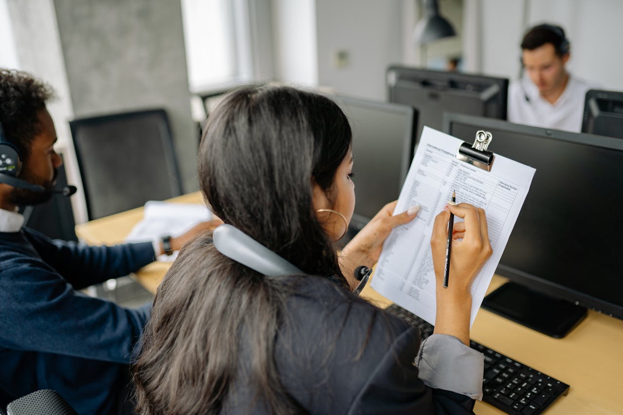 about-02 Focused call center employee reviewing documents while on a call in an office setting.